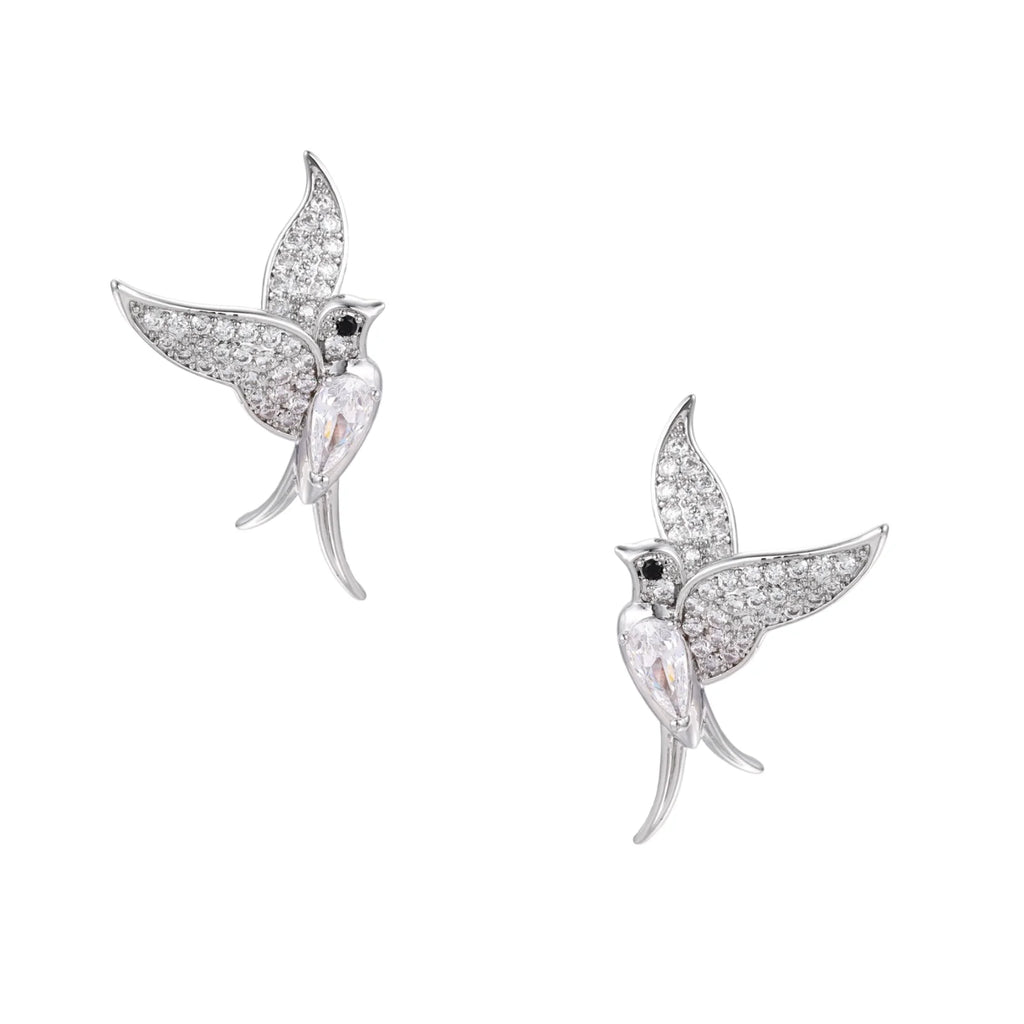 Pair of white gold-plated hummingbird stud earrings with pavé zirconia stones and teardrop crystal bodies on cream background
