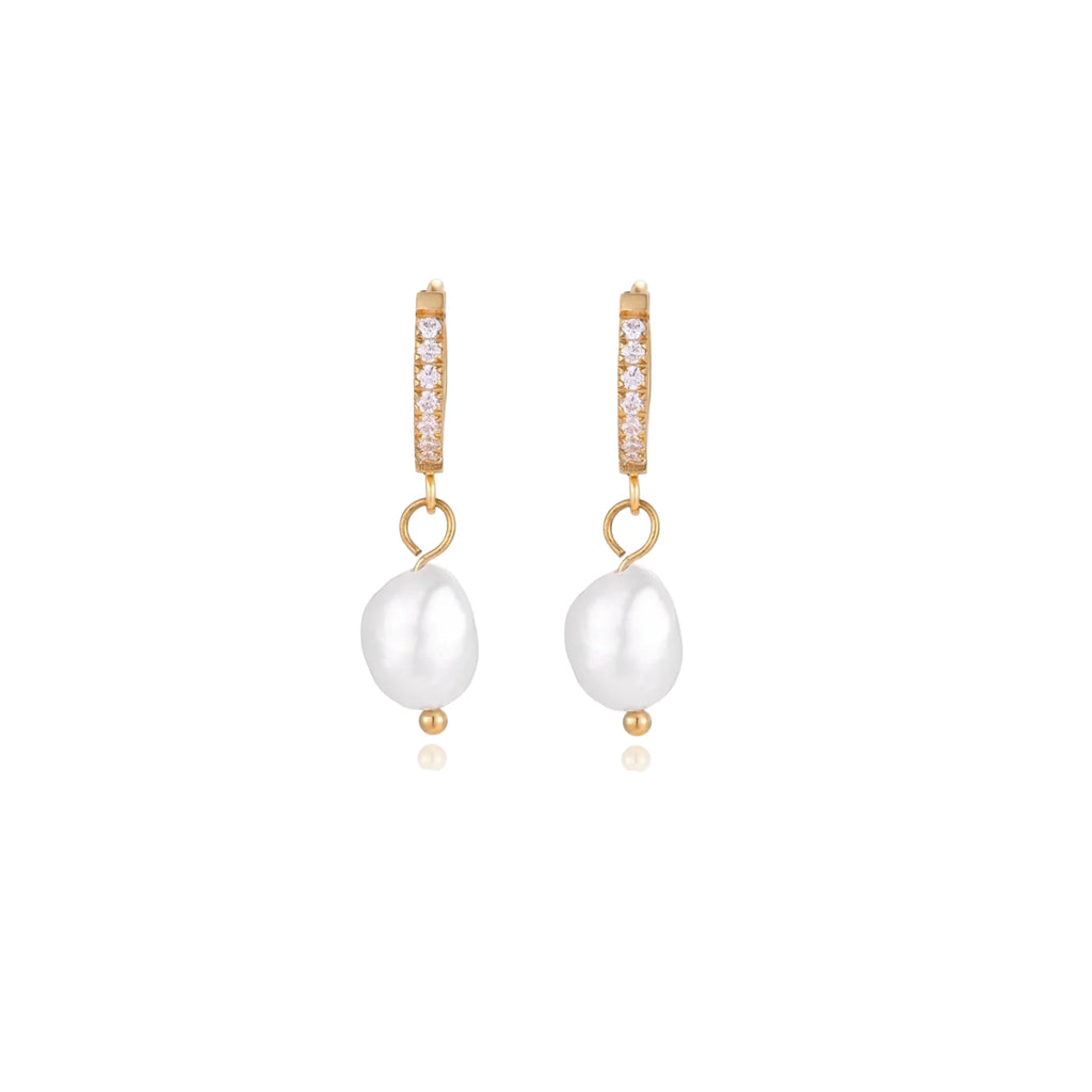 Gold huggie hoop earrings with pavé crystals and white freshwater pearl drops on cream background