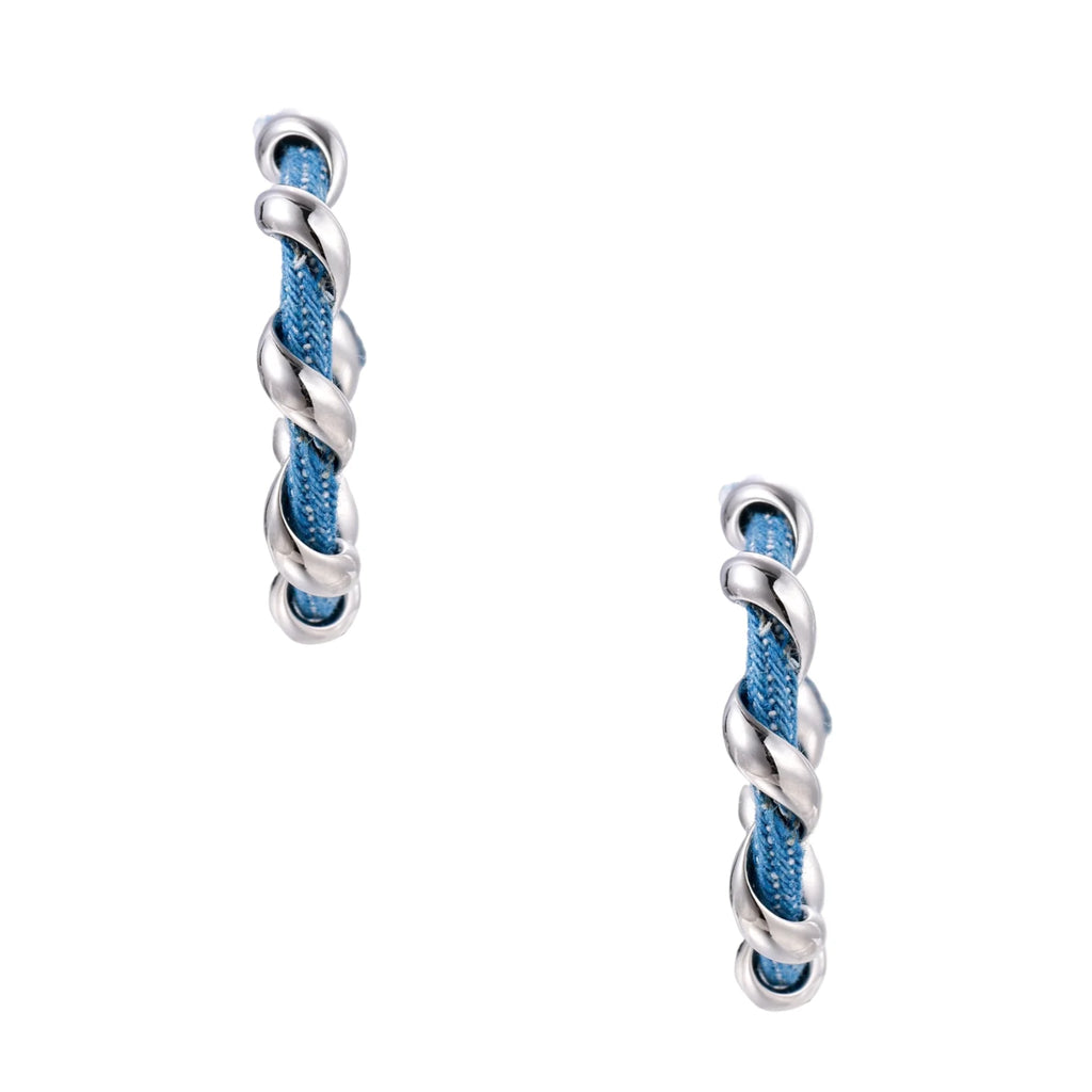 White gold-plated hoops intertwined with blue denim fabric in a twisted rope design on cream background.