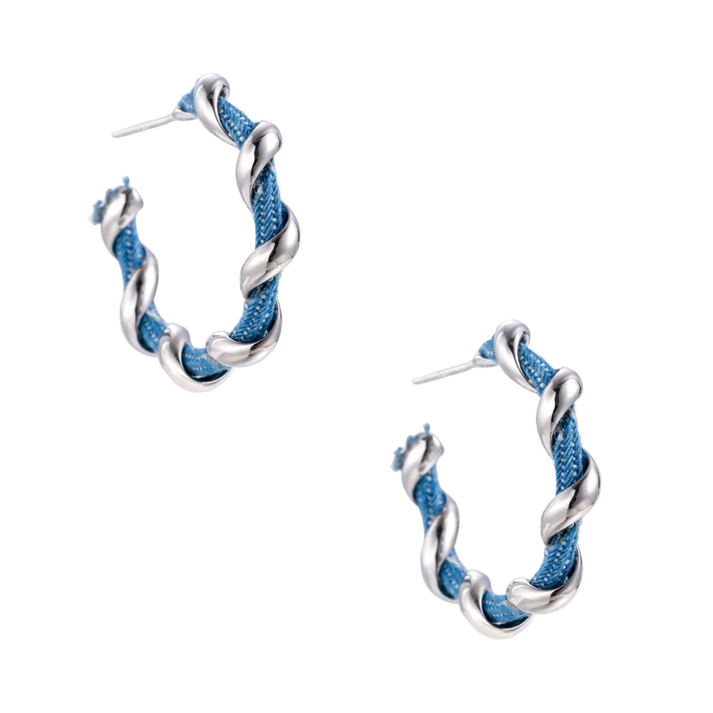 White gold-plated hoops intertwined with blue denim fabric in a twisted rope design on cream background.