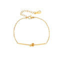 Delicate gold chain bracelet with minimalist bar and centered knot detail on cream background
