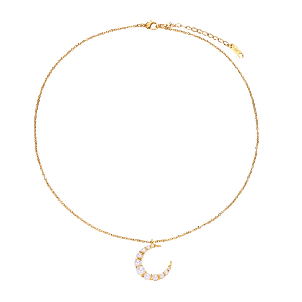Gold crescent moon pendant with graduated white pearls on delicate chain against cream background