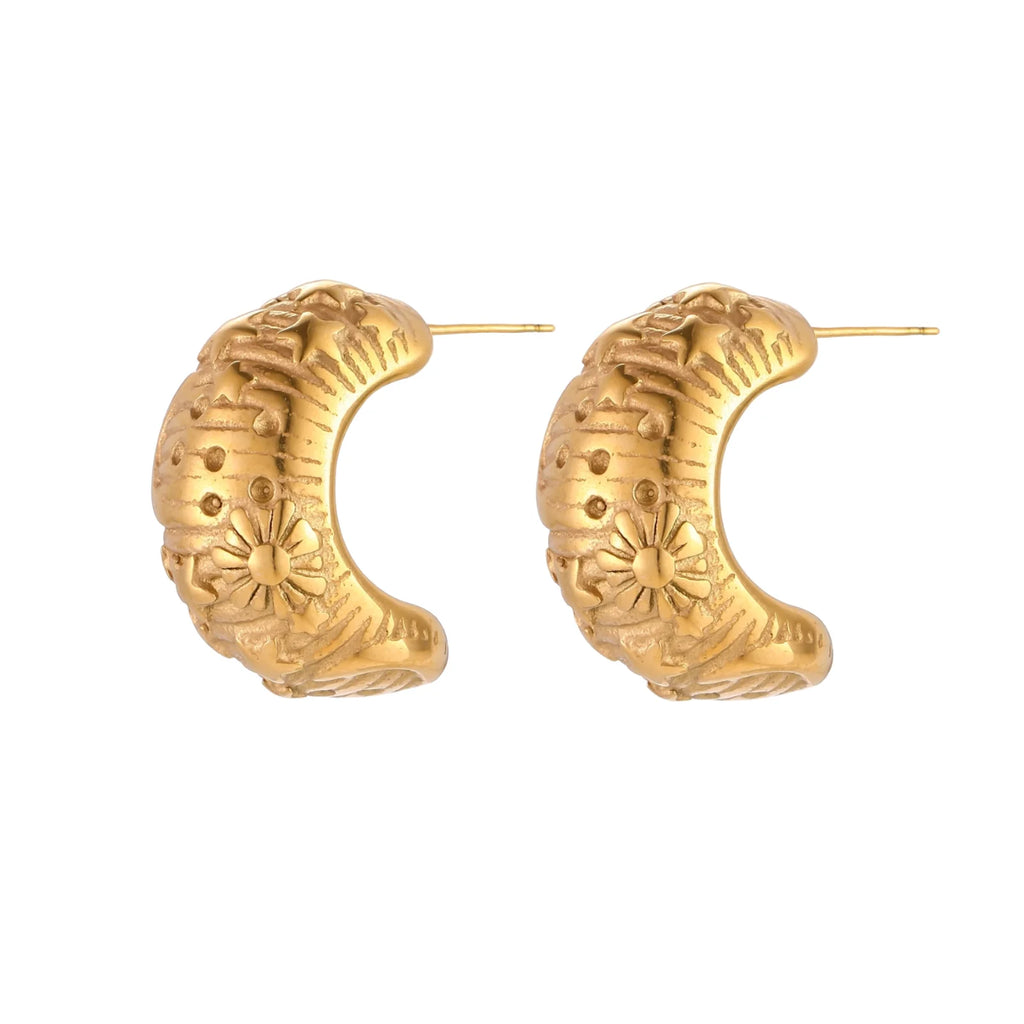 Gold-plated chunky hoop earrings with sun and star engravings on white background, showing detailed celestial pattern work.