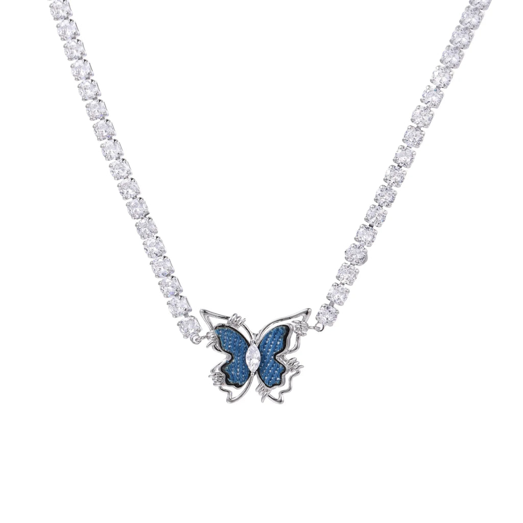 White gold plated tennis necklace with blue denim butterfly pendant and clear zirconia stones on cream background