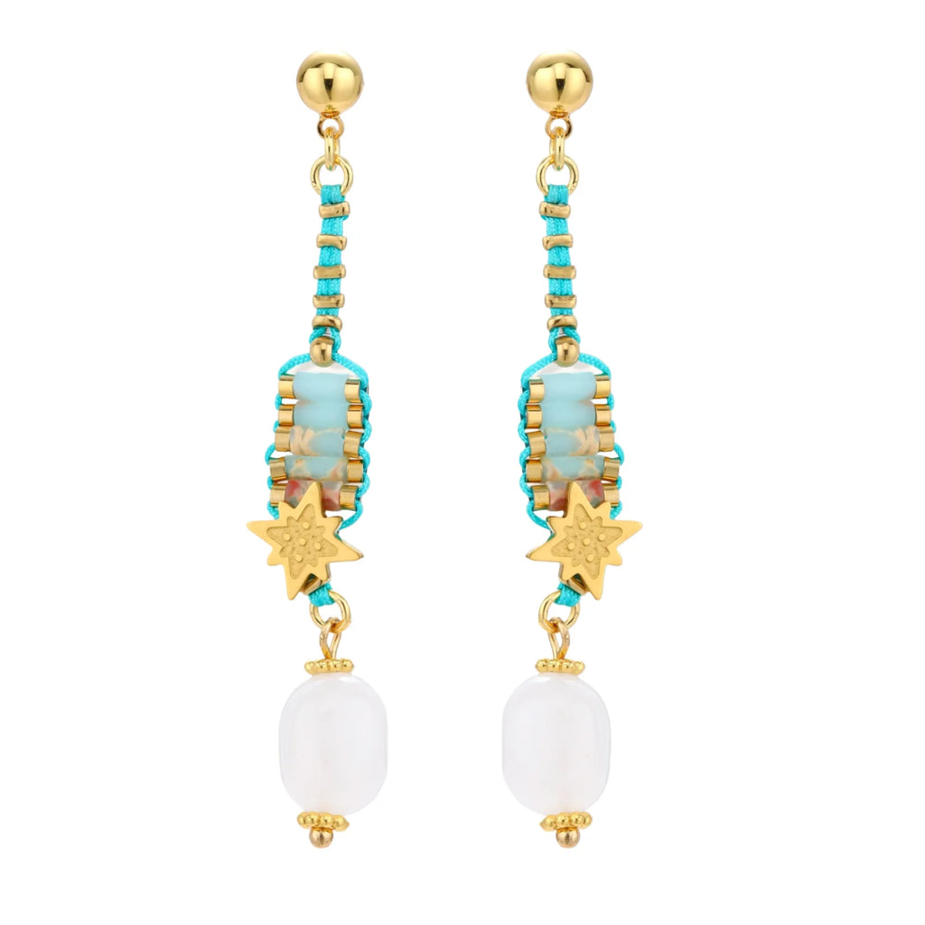 Gold-plated dangle earrings with turquoise threading, star charms, and white pearl beads against cream background.